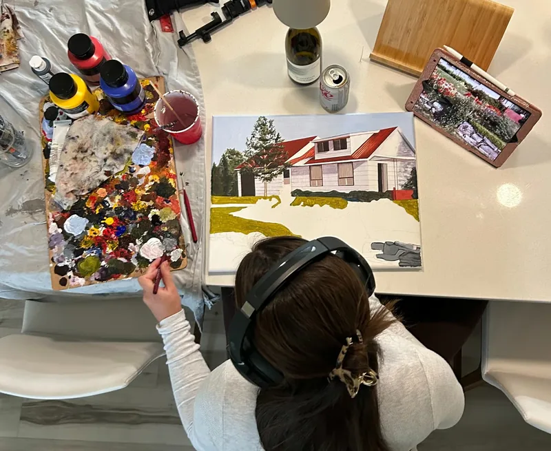 Kenzie painting a red-roofed house at her kitchen table